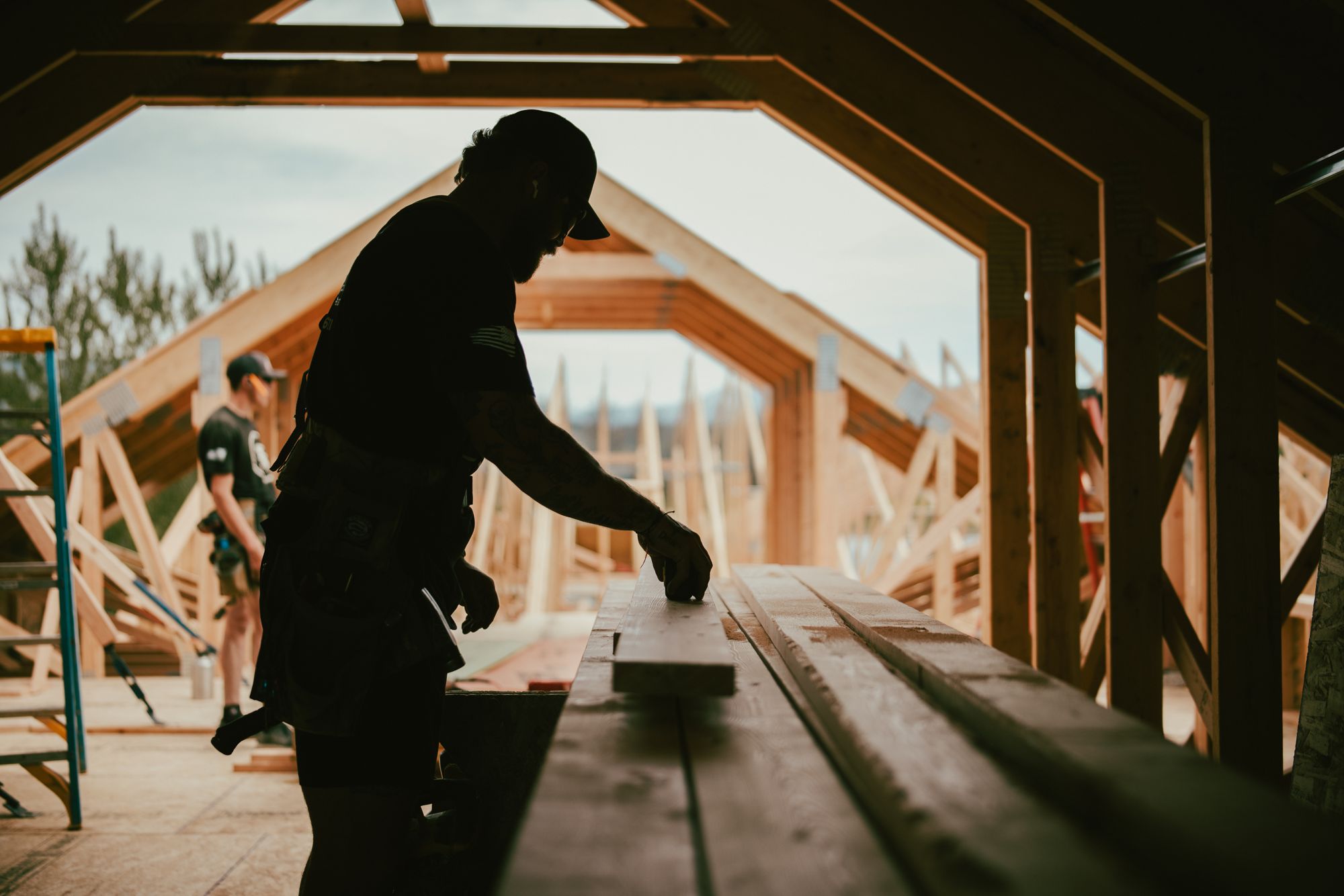 An IB carpenter at the saw, framed against the open gable